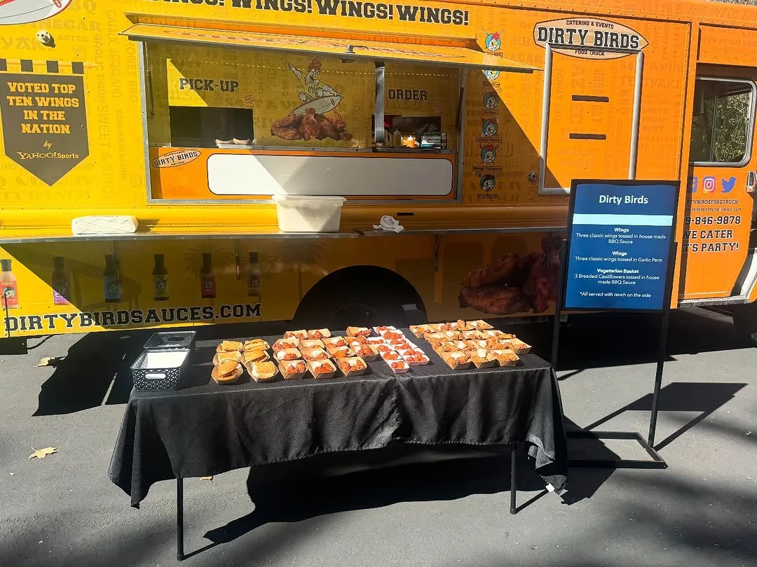 The orange Dirty Birds food truck beside a table at an outdoor event